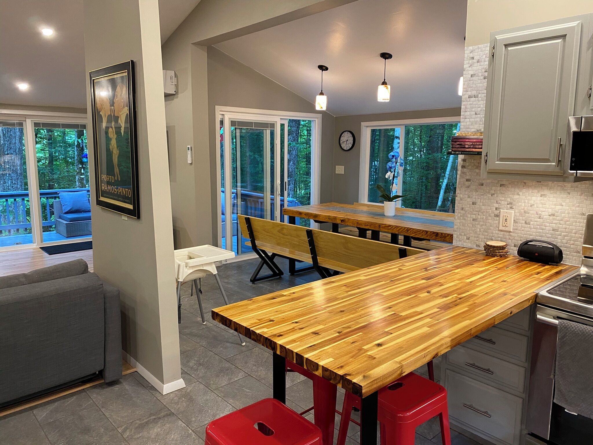 A modern kitchen with a wooden island, red stools, and a view of the outdoors through large windows.