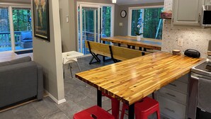 Une cuisine moderne avec un îlot central en bois, des tabourets rouges et une vue sur l’extérieur grâce à de grandes fenêtres.