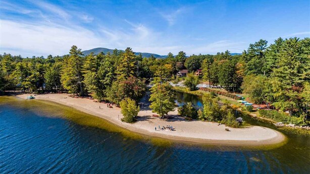 Une propriété au bord du lac, dotée d’une plage de sable, d’une forêt dense et d’un petit bâtiment.