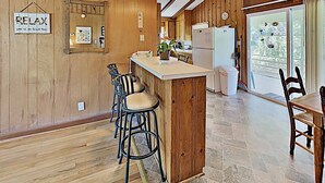 Una cocina acogedora con paredes de madera, una isla central con taburetes de bar, un refrigerador y vistas a través de un ventanal.