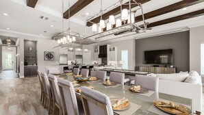 A modern dining area with a glass table, grey upholstered chairs, and a chandelier. - Reunion Fantasy | Games Room, Secret Playroom, English Pub Bar (Kissimmee)