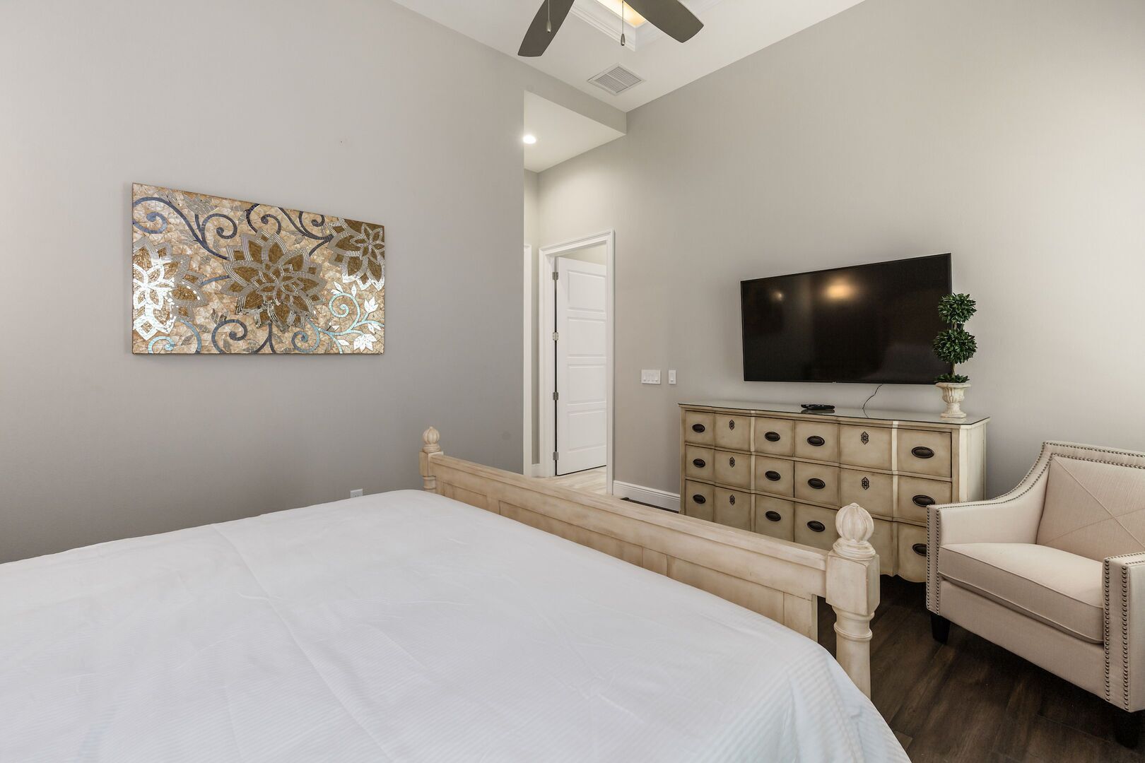 A bedroom with a bed, a dresser, a television, and a decorative wall piece.