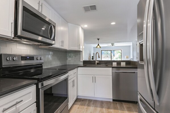 Enjoy cooking in this well-equipped kitchen with stainless steel appliances, white cabinetry, and a black countertop.