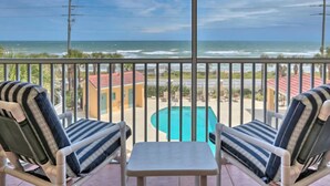 A balcony with two striped lounge chairs and a small table, overlooking a swimming pool and a view of the ocean. - NEW !  Ocean Front Paradise  @  South Beach Condos with Amazing Views !  (Flagler Beach)