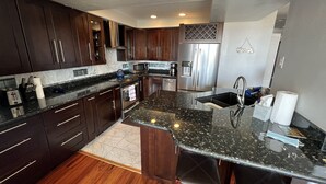 A modern kitchen with dark wood cabinets, stainless steel appliances, a granite countertop, and a bar area with stools. - Ocean View from Living Room & porches -last min special for Nov and Dec!  (Solana Beach)