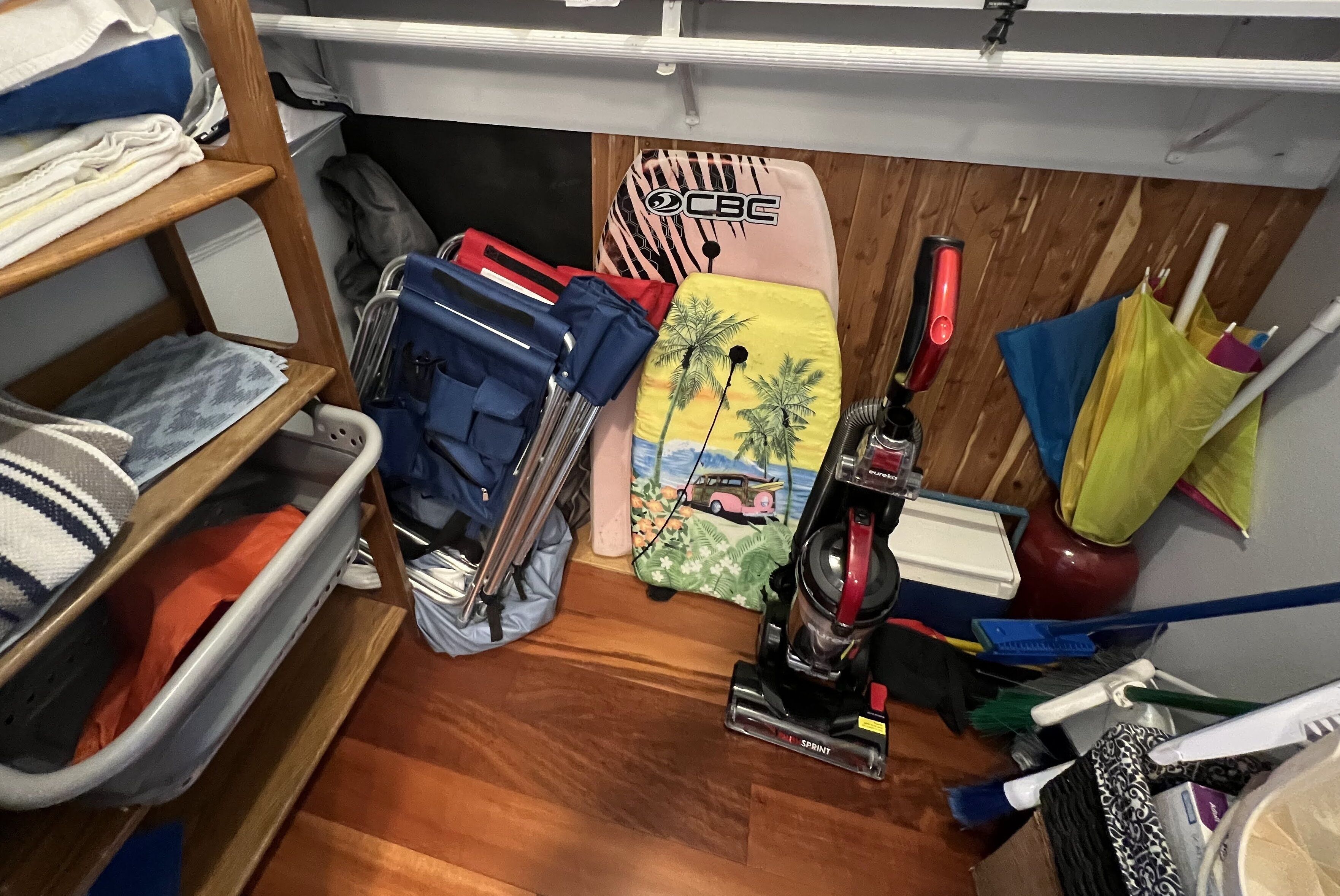 Een kleine opbergruimte met planken, een stofzuiger en schoonmaakmiddelen.