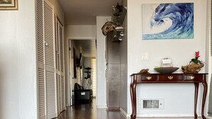 A hallway with wooden flooring, a dark rug, a wooden console table with decorative items, and a wall-mounted painting. - Ocean View from Living Room & porches -last min special for Nov and Dec!  (Solana Beach)
