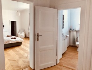 A hotel room with a bed, a chair, a bathroom with a toilet and sink, and a door leading to another room. - Heart of Bratislava-Blue Church views-Sleeps 5-6. (Bratislava)