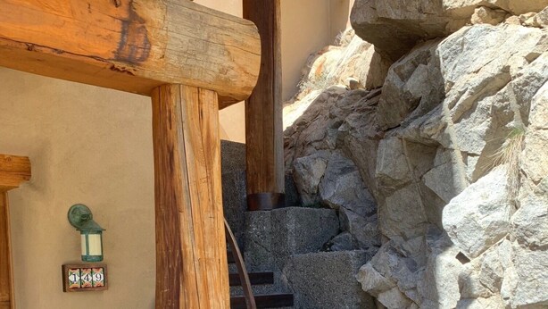 Una escalera de madera con un muro de piedra a un lado y un muro beige al otro.
