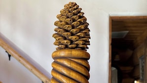 Una escalera de madera con diseño en espiral y un adorno de piña en la parte superior.