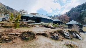 Un albergue rústico con varias tiendas de campaña y un pequeño edificio, ubicado en un paisaje natural y montañoso.