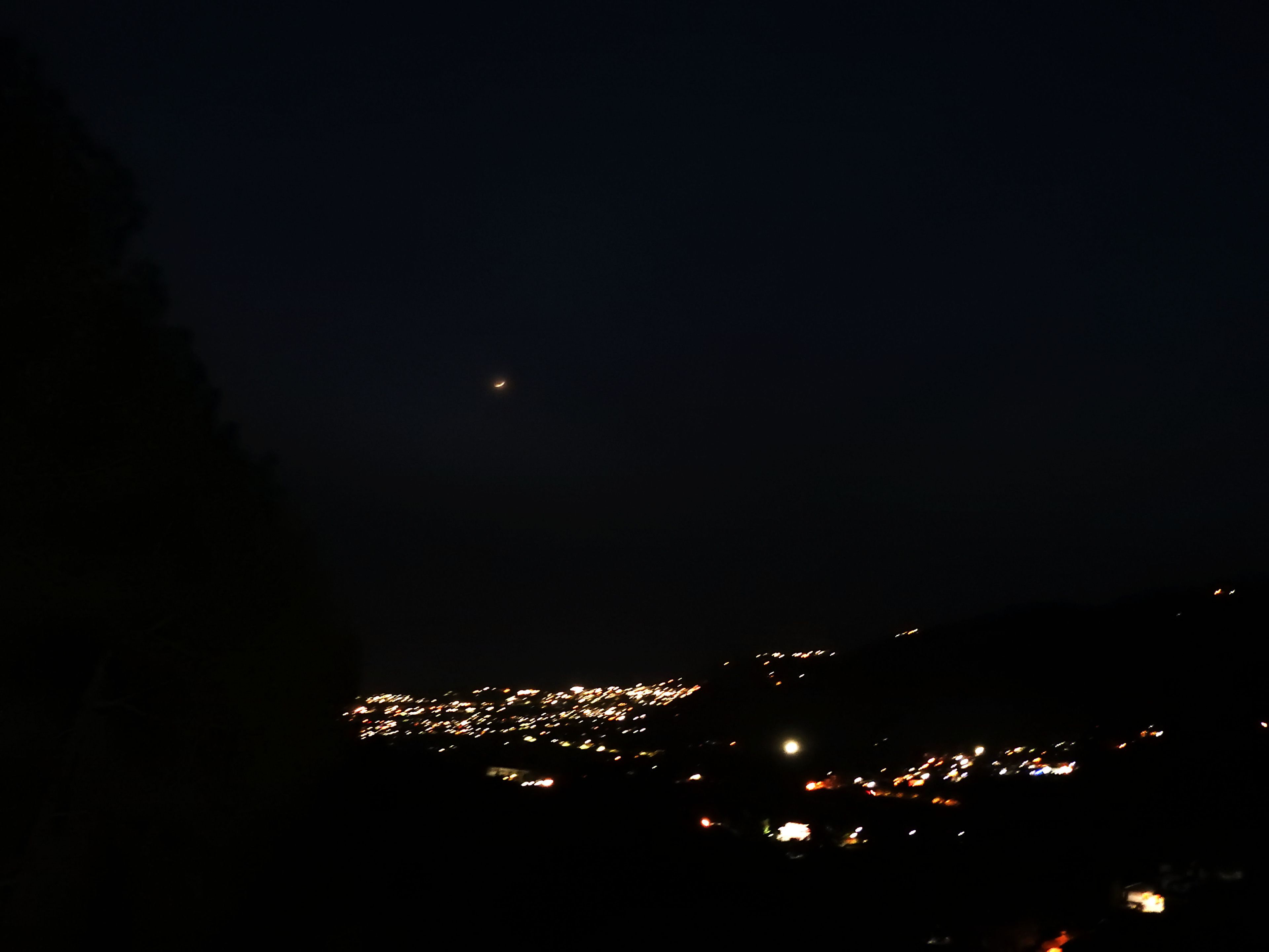 Udsigt over byen om natten, med en halvmåne på himlen.