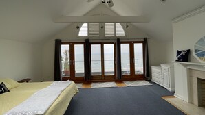 Ein Schlafzimmer mit einem großen Bett, einem Deckenventilator, einem Kamin, Meerblick durch eine Schiebetür und einem Dachfenster.