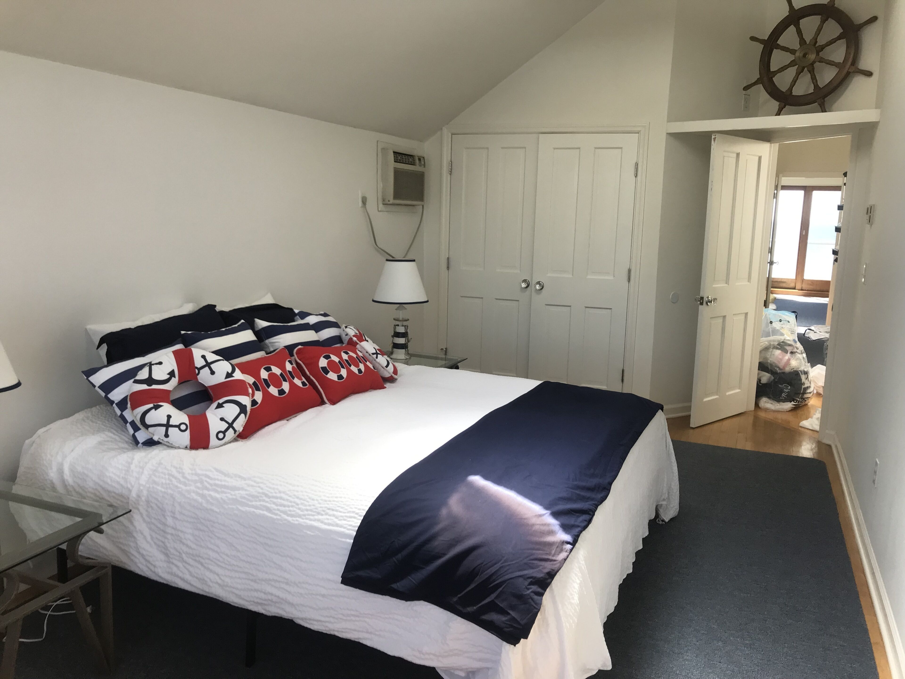 A bedroom with a bed, a lamp, a wardrobe, and a door leading to another room.