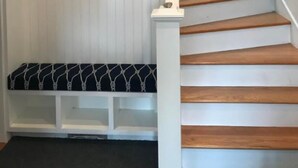 Eine Treppe mit Holzboden und weißen Geländern, die zu einer Empore mit weißem Wandverkleidung und einer Bank mit Kissen in Schwarzweiß führt.