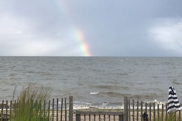 A beach with a wooden fence, a striped beach umbrella, and a rainbow in the background. - Stunning direct waterfront beach house! (Fairfield)