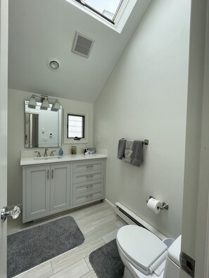 A modern bathroom with a skylight, white fixtures, a large mirror, and a toilet. - Stunning direct waterfront beach house! (Fairfield)