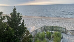 Ein Strand mit Holzlattenzaun, Stühlen und Blick auf das Meer.