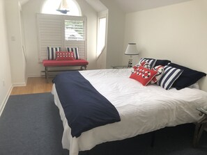 A bedroom with a large bed, a bench with pillows, a lamp, and a window with blinds. - Stunning direct waterfront beach house! (Fairfield)