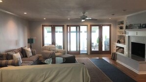 Ein modernes Wohnzimmer mit Sofa, Sessel und einem Schlafsofa. Es gibt einen Kamin und einen Deckenventilator.