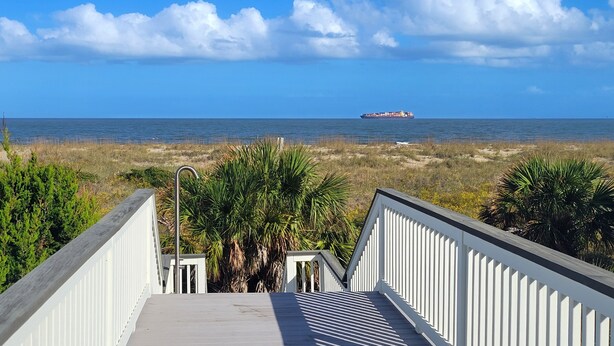 A wooden staircase leading to a beach with a cargo ship in the distance.
