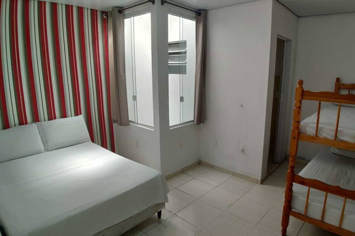 A bedroom with a bed, a bunk bed, a window with curtains, and a door.