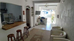 A modern kitchen with a wooden countertop and bar stools, a dining area with a table and chairs, and a view of the street through a large window.