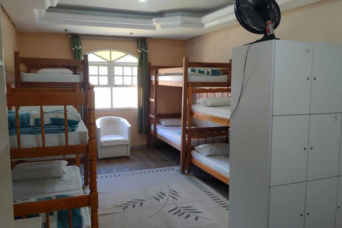 A dormitory room with bunk beds, a white chair, a fan, and a wardrobe.