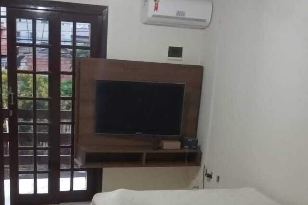 Une pièce comprenant un lit, un téléviseur fixé au mur, une petite table et une porte donnant sur un espace extérieur.