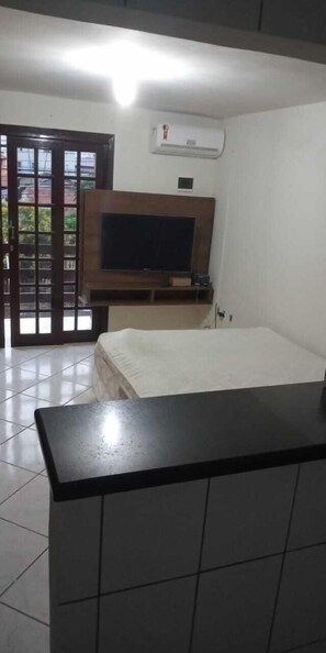 A room with a bed, a TV mounted on the wall, a small table, and a door leading to an outdoor area. - Pousada Triunfo (Balneário Camboriú)