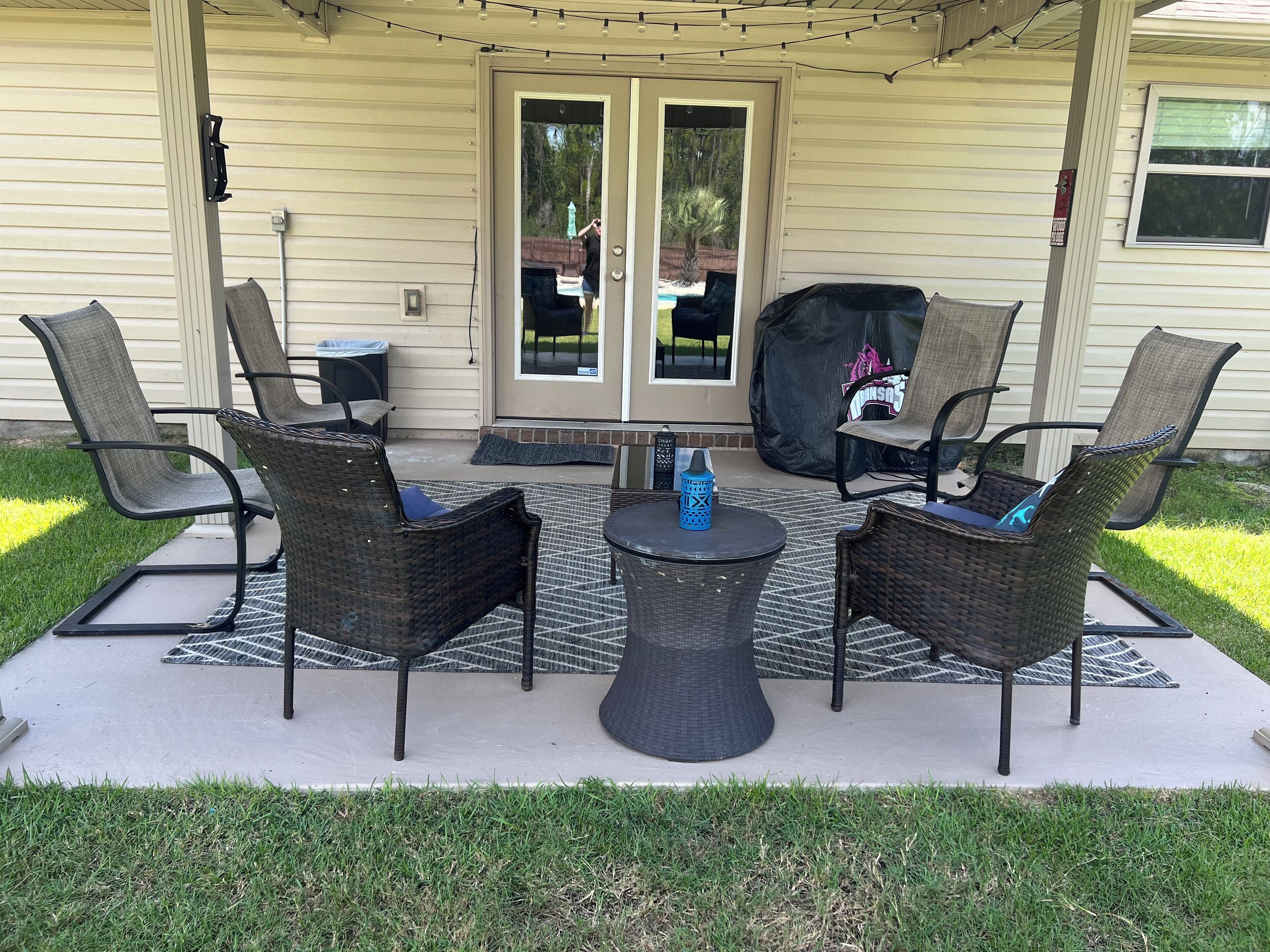 Eine Terrasse im Freien mit Korbmöbeln, einem Tisch und einem überdachten Grill.