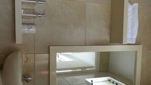 Un baño con lavamanos con cristal, un perchero y un espejo.