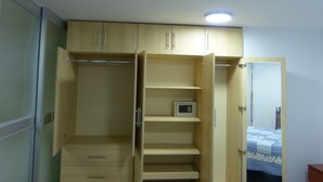 Una habitación con un armario de madera, una pequeña estantería y una cama con colcha azul y blanca.