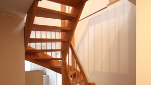 Un escalier en bois, surmonté d’une structure en verre, mène à une pièce dont un des murs est blanc et qui possède une fenêtre.