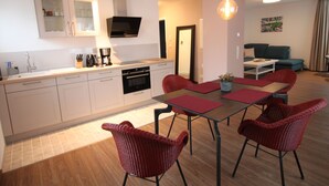 Une cuisine moderne avec des armoires blanches, un four encastré et un coin repas comprenant une table et des chaises rouges.