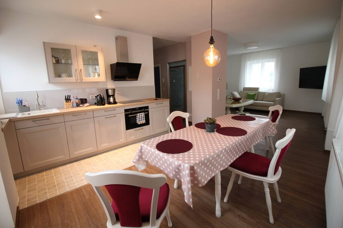 Una cocina moderna con armarios blancos, una mesa de comedor con sillas rojas y un televisor sobre la encimera.