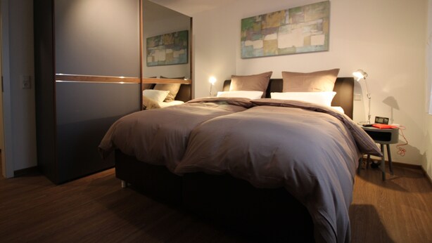 Une chambre moderne avec un grand lit, des tables de chevet, une armoire et des œuvres d’art abstraites accrochées au mur.