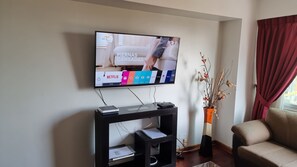 A living room with a flat-screen TV mounted on the wall, a black entertainment unit below, a beige sofa, and a decorative vase with branches. - Great location at Miraflores  (Lima)