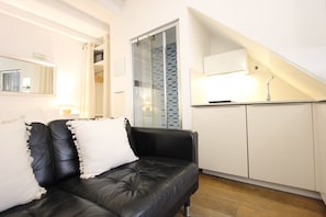 Un salon moderne avec un canapé en cuir noir, un coussin blanc et une cloison en verre.
