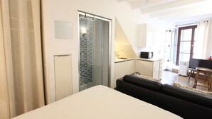 Una habitación de hotel moderna con cama, un pequeño sofá, cabina de ducha de vidrio, kitchenette y vistas al exterior.