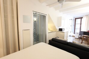 A modern hotel room with a bed, a small sofa, a glass shower enclosure, a kitchenette, and a view of the outside. - La lonja - old town Palma (Palma de Mallorca)