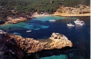 A coastal area with rocky terrain, clear blue waters, and boats.