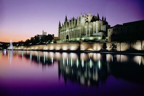 A historic building with a prominent tower, situated by a calm body of water reflecting the structure.