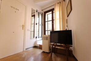 Habitació amb terra de fusta, aire condicionador blanc, televisió sobre un suport de fusta i porta amb nansa de bronze.