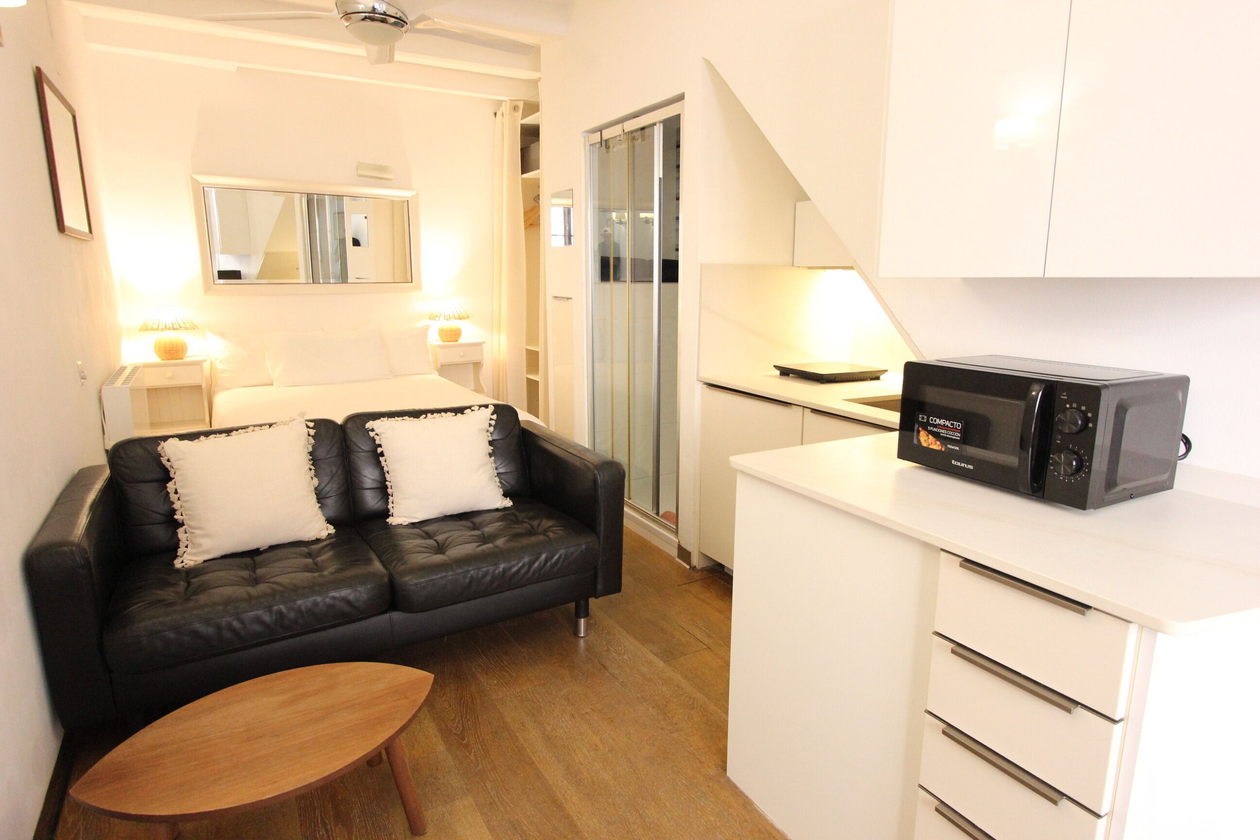 A compact kitchenette with a microwave, a small table, and a sofa with cushions.