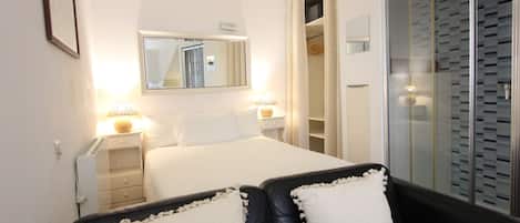 Une chambre d’hôtel comprenant un lit, des tables de chevet, un miroir, une armoire et un coin salon avec des coussins.