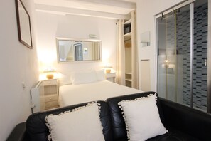 Et hotelværelse med seng, natborde, et spejl, et garderobeskab og et siddeområde med puder.
