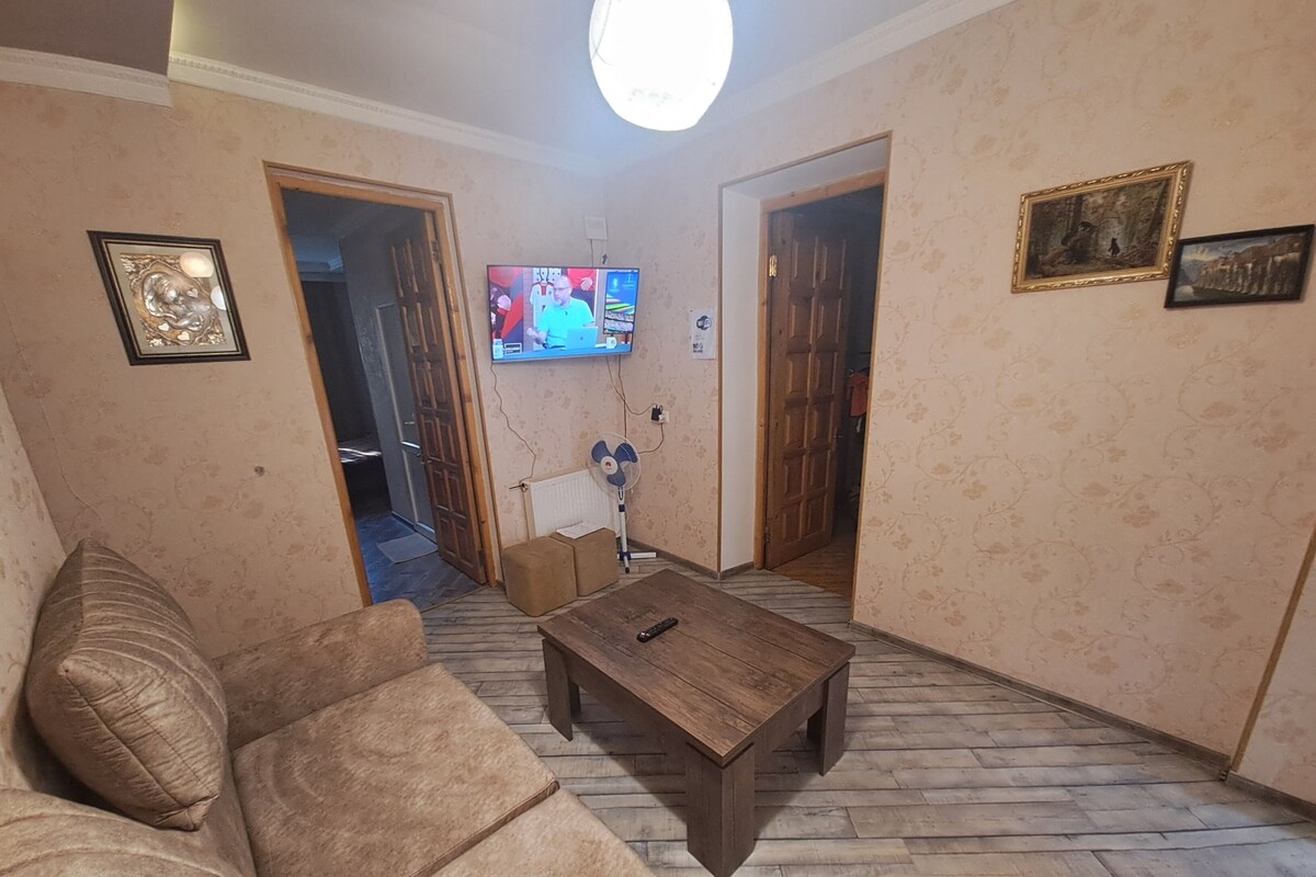A living room with a wooden coffee table, a sofa, and a television mounted on the wall.