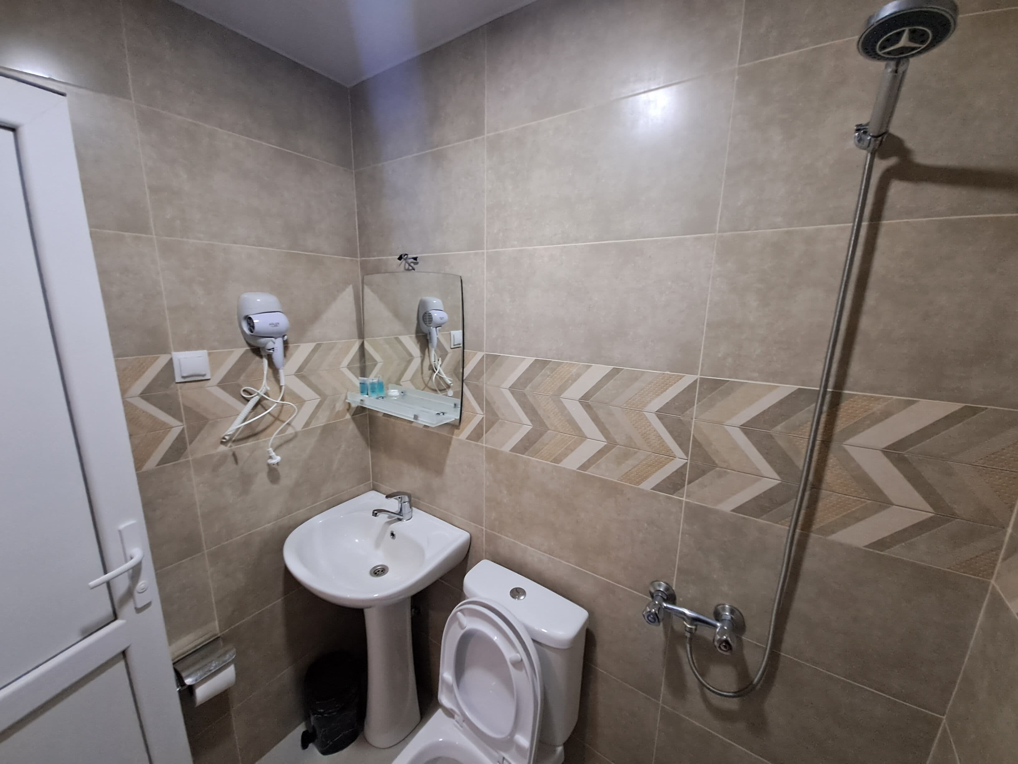 A bathroom with a sink, toilet, and shower. There are hair dryers mounted on the wall.