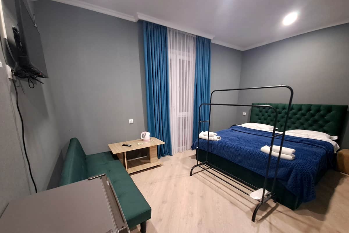 A hotel room with a bunk bed, a small desk with a chair, a green sofa, and a TV mounted on the wall.